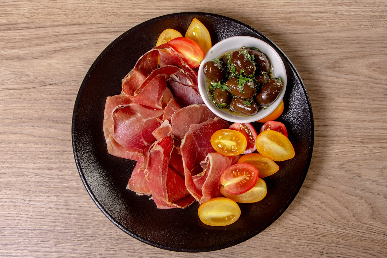 Tasty charcuterie plate featuring cured ham, colorful cherry tomatoes, and marinated olives.